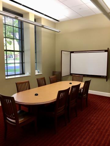 picture of the small meeting room, table with chairs surrounding it, and a dry erase folder