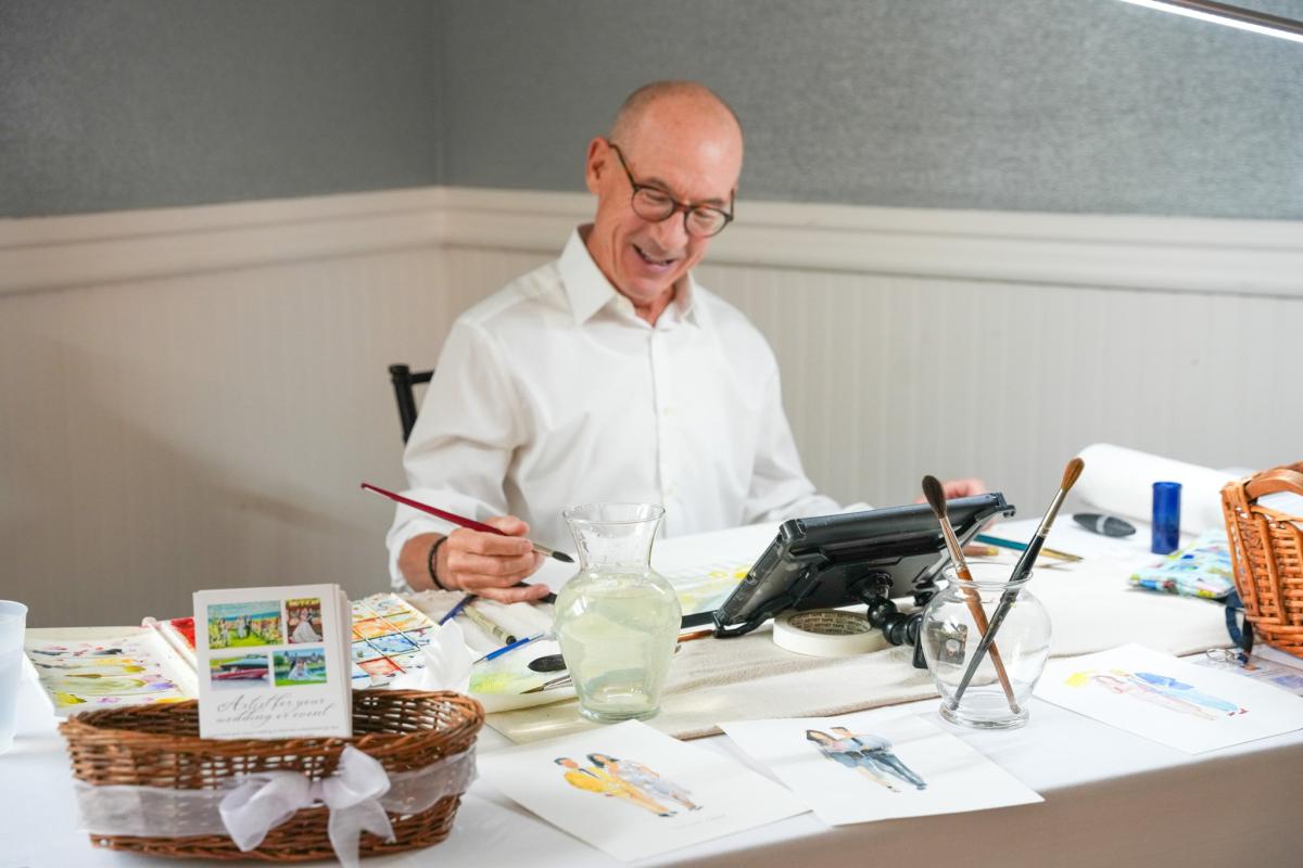 picture of artist patrick wise seated at a table painting with a paintbrush 